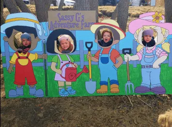 Four children posing behind a colorful farm-themed cutout board with face holes.