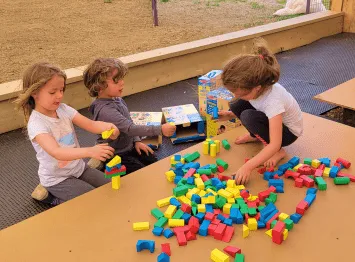 Children playing with colorful building blocks at a table outdoors.